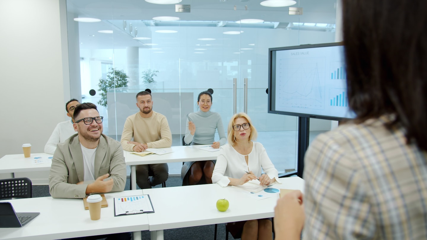 Business professional presenting to diverse attendees in a modern conference room.