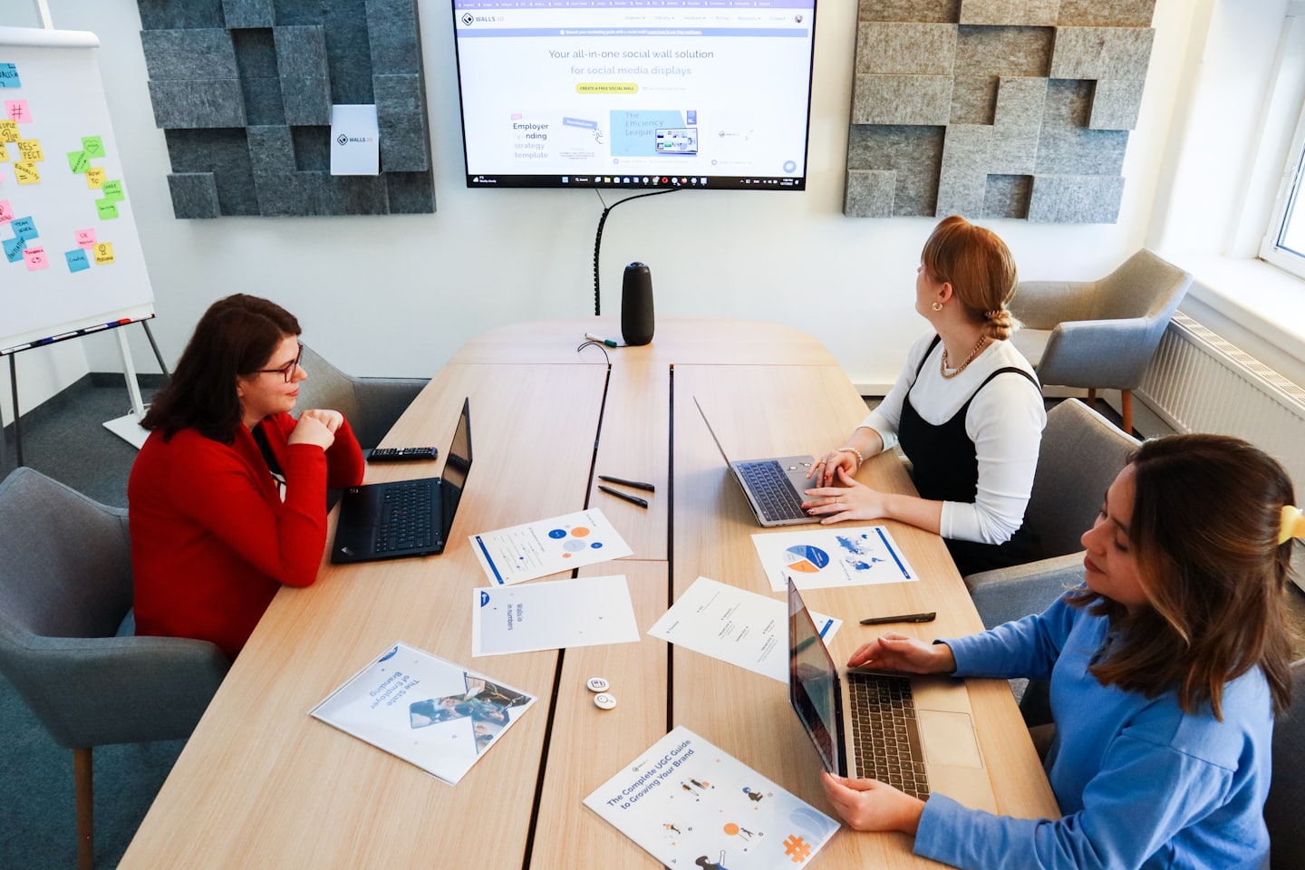 Three women work together on laptops at an office table.
